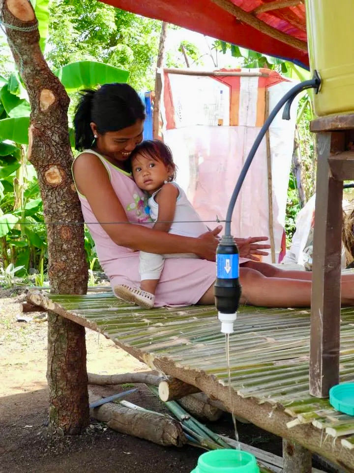 Woman and child sitting beside a household water bucket filter